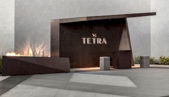 Modern architectural entrance for "TETRA" with sleek lines and minimalistic design elements, featuring a fire element and greenery.