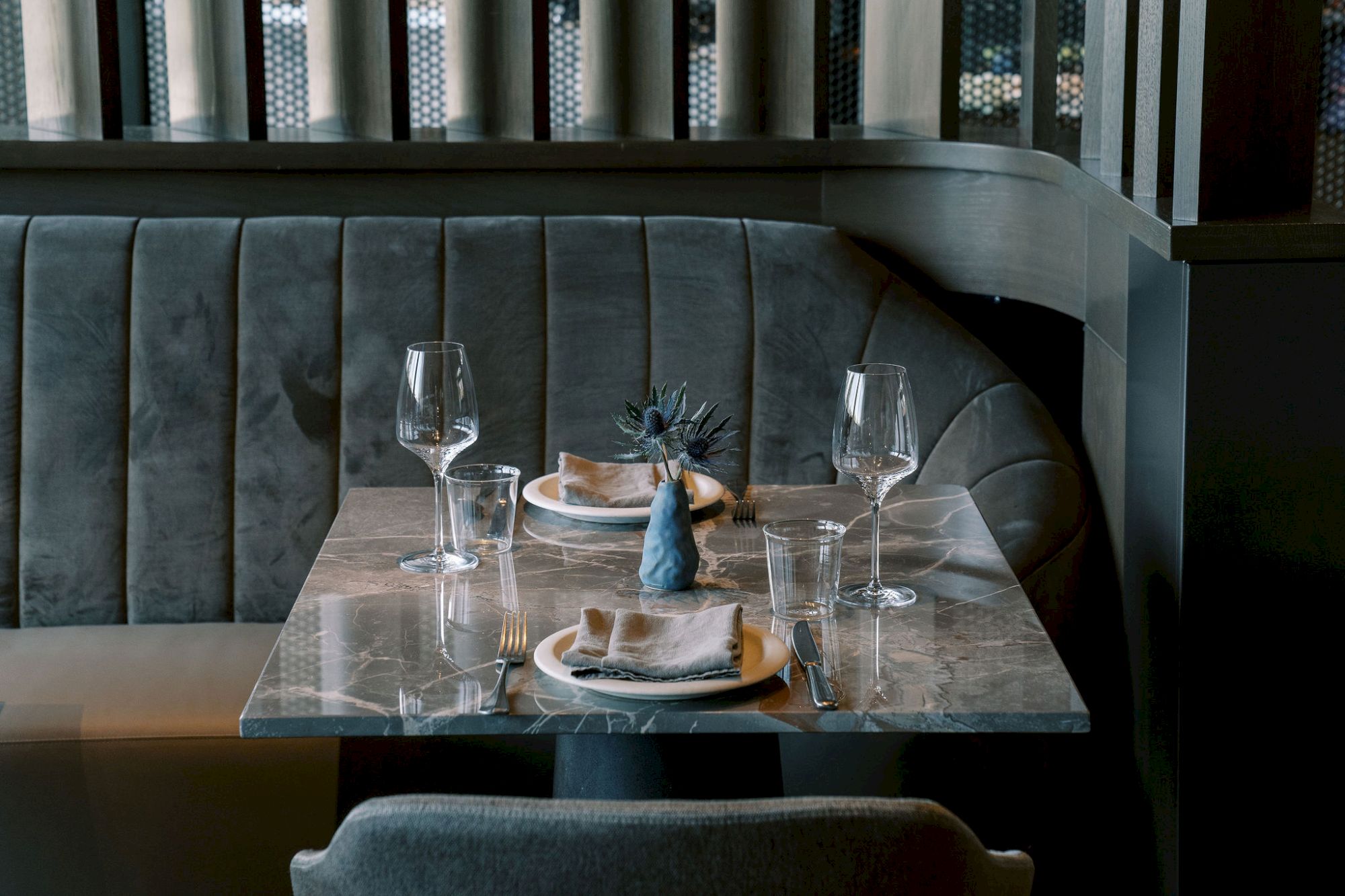 A restaurant table set for two with glassware, plates, napkins, and a small decorative centerpiece in a dimly lit, cozy setting.