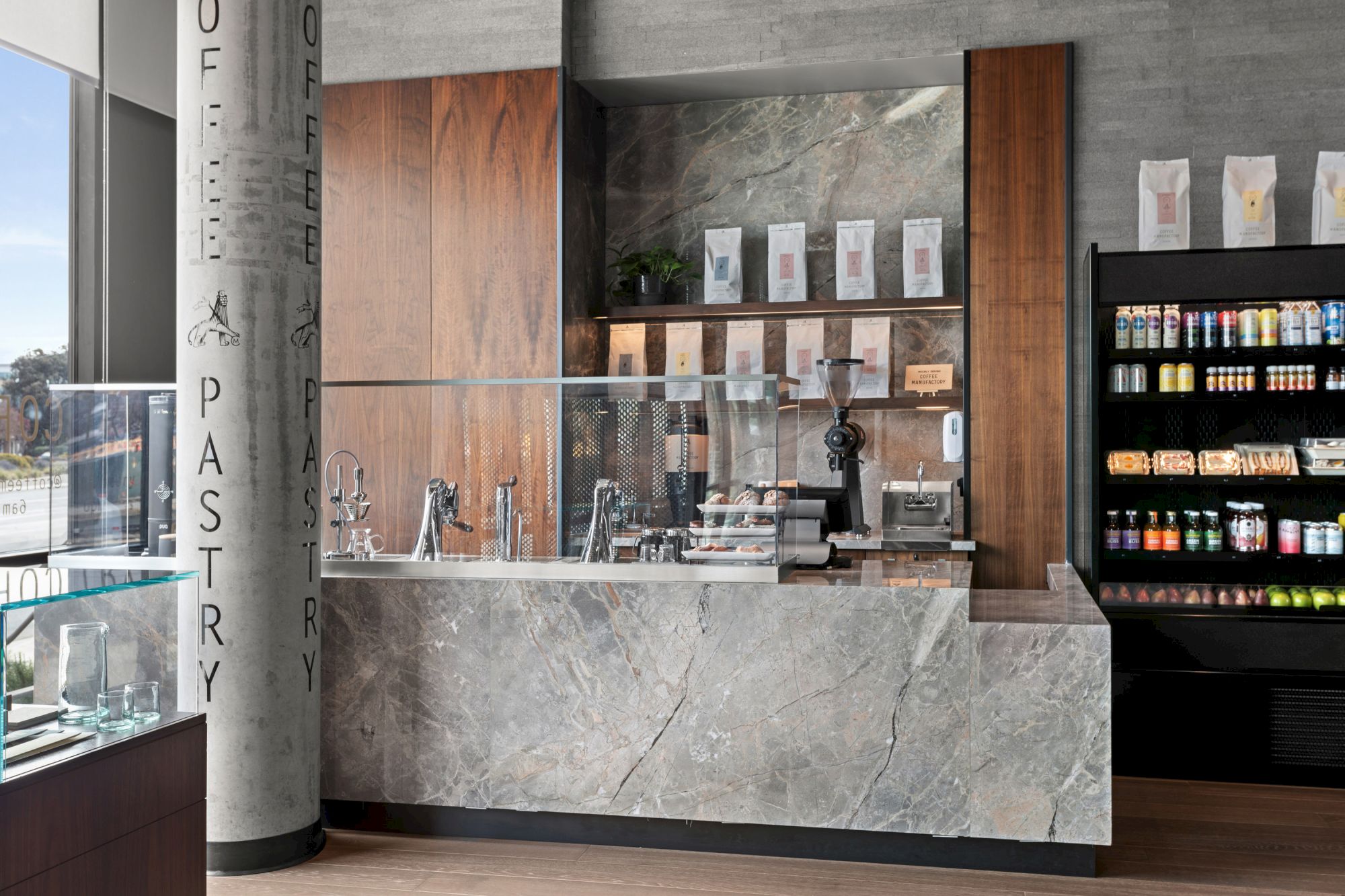 A modern coffee shop counter with a marble finish, coffee machines, and a display of products on shelves and a fridge.