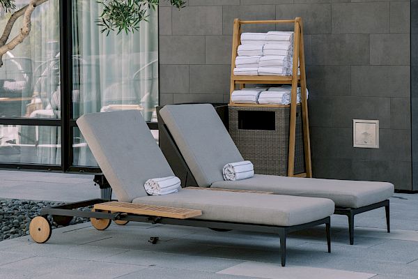 Two outdoor loungers with towels beside a modern building, surrounded by trees under natural light.