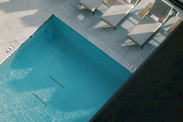 Aerial view of a pool area with lounge chairs aligned beside it, surrounded by potted plants and glass railings.