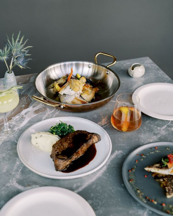 A table with various dishes including meat, fish, and vegetables, alongside drinks and an empty plate.