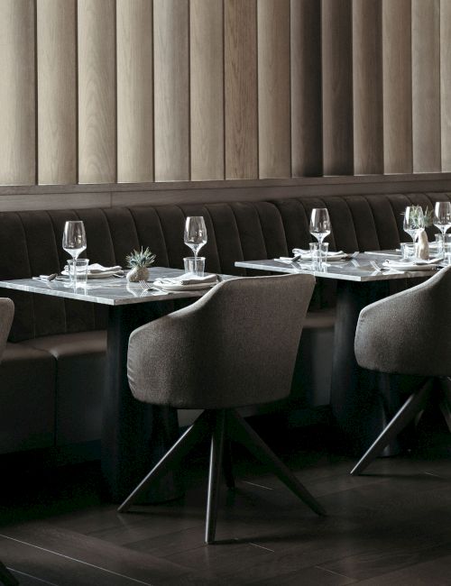 A restaurant setting with modern chairs and tables, set with wine glasses, napkins, and small plants, in a calm, elegant atmosphere.