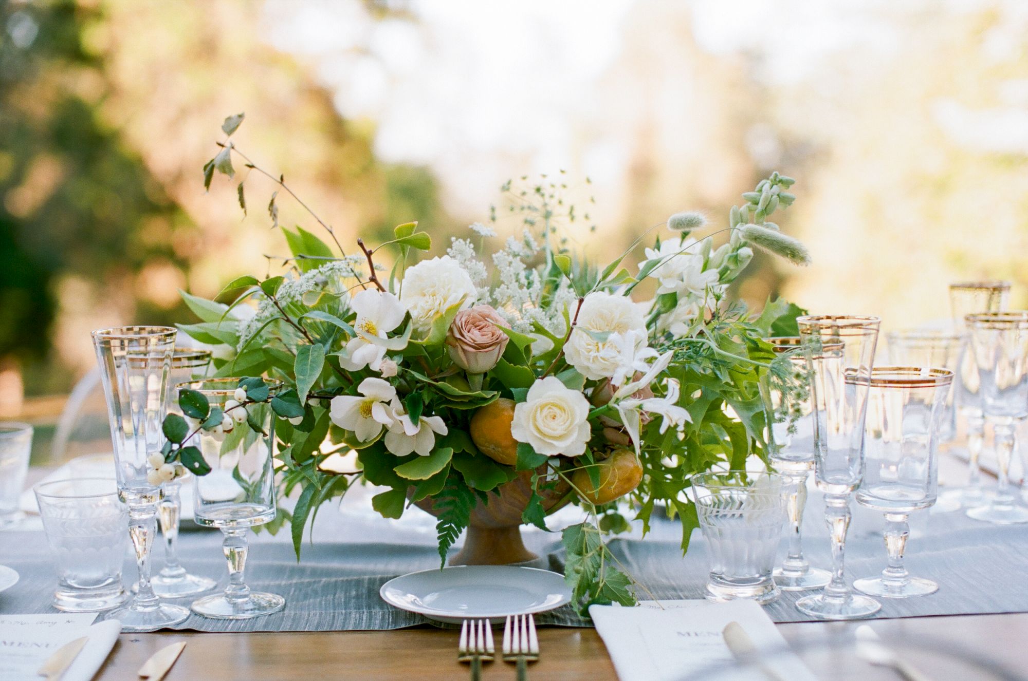 A beautifully arranged centerpiece with flowers and greenery, surrounded by elegant glassware on a set dining table.