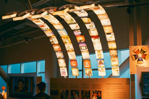 The image shows a display with various illuminated hanging panels, each showing different designs and images, inside a modern exhibition space.