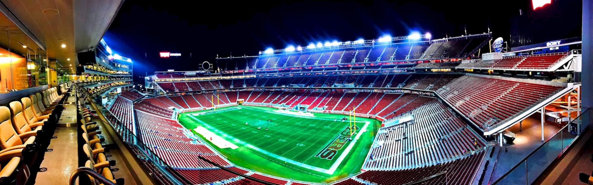 A brightly lit football stadium with empty stands and neatly maintained field, viewed from a box seating area at night.