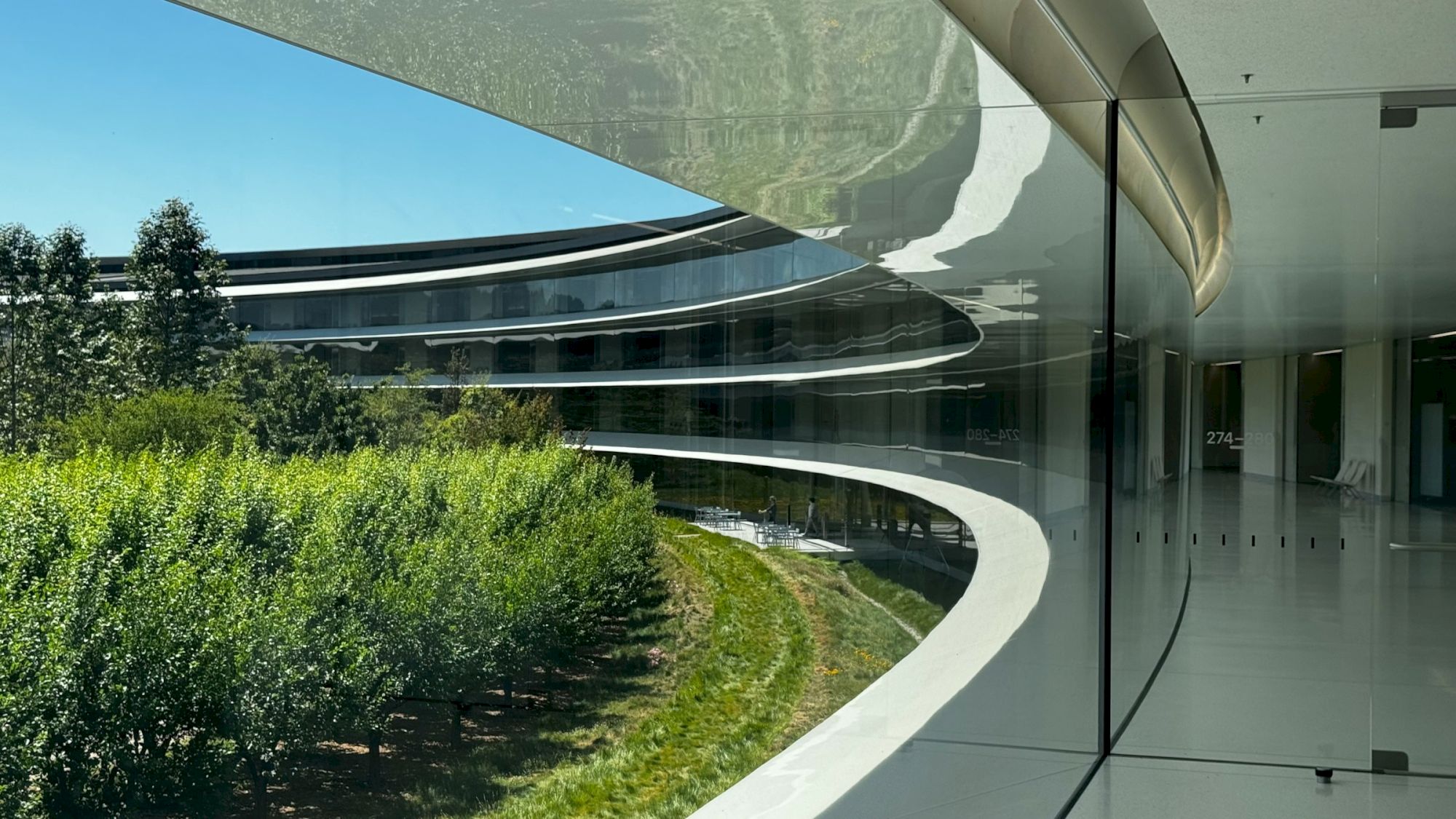 A modern building with curved architecture and glass walls overlooks a landscaped green area, blending nature with urban design.