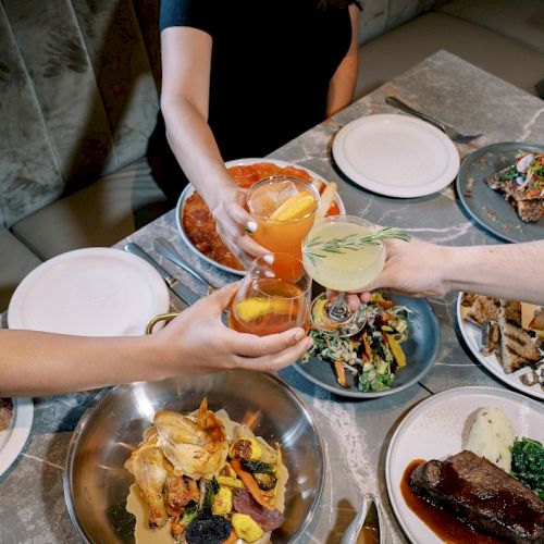 A group is toasting over a table filled with various dishes, including meats, salads, and drinks.