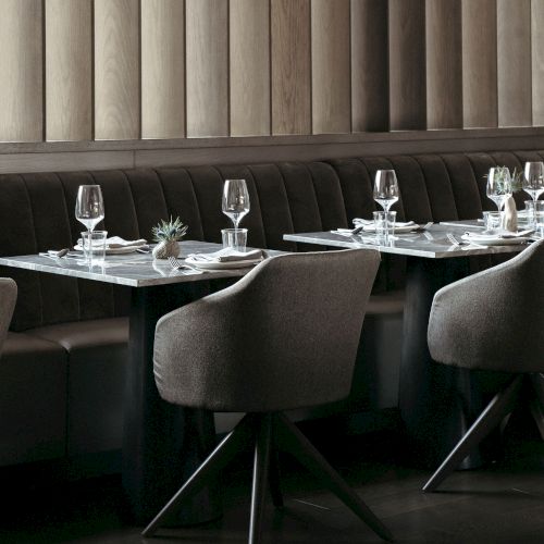 A stylish restaurant interior with elegant tables set with glassware, napkins, and small plants, against wood paneling.