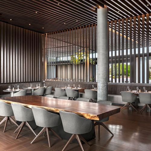 A modern restaurant interior with wooden decor, grey chairs, and tables set with glassware, creating a stylish and elegant atmosphere.