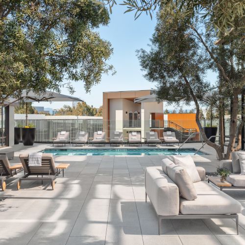A luxurious outdoor space featuring a pool, lounge chairs, sofas, trees, and a fire pit, creating a serene and stylish setting.